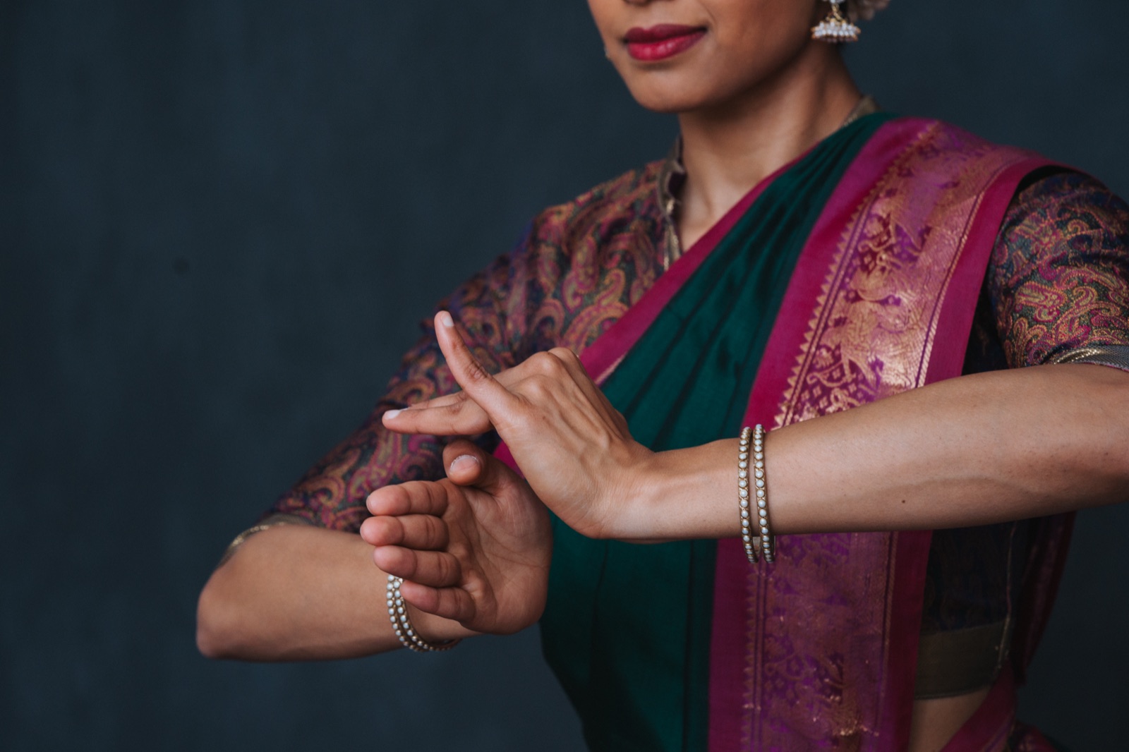 Close-up of Vertika's hands forming a bharatanatyam hasta mudra, wearing a green and magenta silk saree.